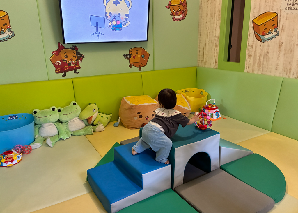 赤ちゃんスペースのクッションブロックに登る1歳